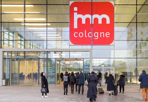 Besucherinnen und Besucher mit Gepäck gehen durch den Eingang der Messehalle zur imm cologne in Köln.