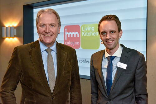 Zwei lächelnde Männer in Anzug und Krawatte stehen nebeneinander vor einer Präsentationsfolie mit den Logos von „imm cologne“ und „Living Kitchen“ in einem Konferenzraum.