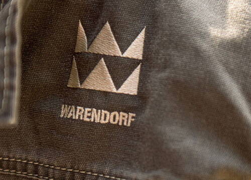 Genähter Stoffausschnitt mit aufgedrucktem geometrischem Logo und dem Schriftzug „Warendorf“