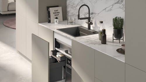 Minimalistische Küche mit Marmorarbeitsplatte, schwarzer Spüle, offenem Auszugsschrank und dekorativen Accessoires wie Kochbüchern, Ölflaschen und einem Kräutertopf.