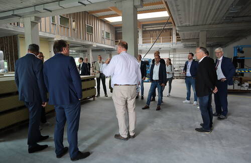 Gruppe von Geschäftsleuten lässt sich in einer großen, noch im Bau befindlichen Industriehalle durch einen Mitarbeiter die Baustelle erklären