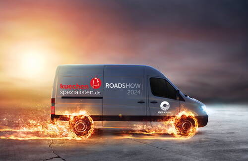 Blauer Lieferwagen der „kuechenspezialisten.de“ Roadshow 2024 rast über Asphalt, während seine Räder in leuchtenden Flammen stehen und der Himmel im Hintergrund dramatisch im Sonnenuntergang leuchtet.