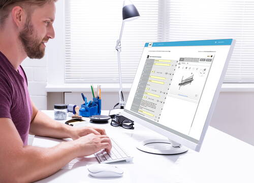 Mann arbeitet konzentriert an einem Schreibtisch und bedient eine Software mit technischen Tabellen und Produktabbildungen auf einem großen Computerbildschirm.