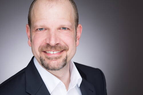 Lächelnder Mann im Anzug mit weißem Hemd vor neutral grauem Hintergrund in einem professionellen Portraitfoto