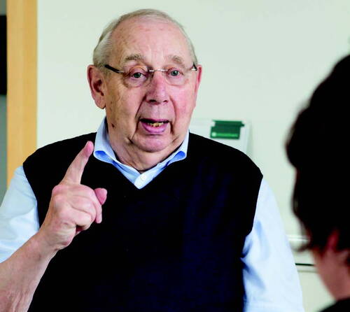 Älterer Mann mit Brille erklärt engagiert etwas und hebt dabei mahnend den Zeigefinger einer zweiten, nur teilweise sichtbaren Person gegenüber.