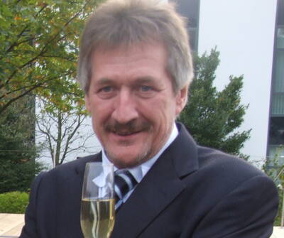 Mittelalterlicher Mann im Anzug hält lächelnd ein Glas Sekt im Freien vor einem modernen Gebäude