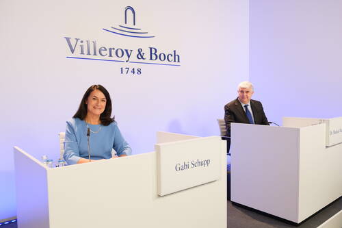 Gabi Schupp und ein weiterer Manager sitzen lächelnd an getrennten Rednerpulten in einem hellen Konferenzraum vor dem Villeroy-&-Boch-Logo.
