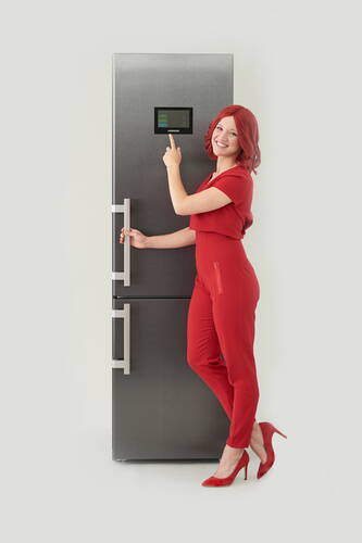 Frau in rotem Overall bedient lächelnd das Touchdisplay eines modernen grauen Kühlschranks
