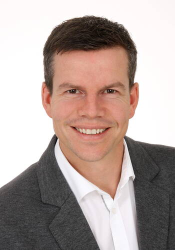 Freundlich lächelnder Mann im Anzug mit weißem Hemd vor neutralem Hintergrund
