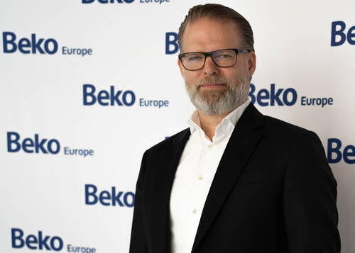 Geschäftsmann mit Brille und grauem Bart im dunklen Anzug vor einer Pressewand mit dem Logo „Beko Europe“