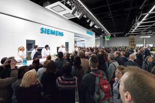 Große Messebesuchergruppe verfolgt eine Live-Kochvorführung an einem hellen Siemens-Stand mit mehreren Köchen vor moderner Küchentechnik.