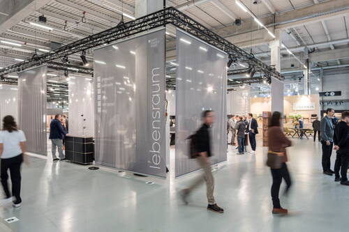 Besucher bewegen sich durch eine moderne Messehalle mit hohen Decken und halbtransparenten Ausstellungstrennwänden, auf denen der Schriftzug „lebensraum“ und weitere Ausstellerangaben zu sehen sind.