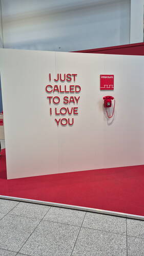 Rote Telefoninstallation auf einer Messewand mit dem Schriftzug „I JUST CALLED TO SAY I LOVE YOU“ über rotem Teppichboden