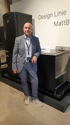 Mann im grauen Anzug präsentiert auf einer Messe eine moderne schwarze Kücheneinrichtung der Designlinie „MattB“
