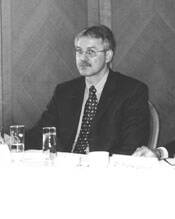 Mittelalter Mann im Anzug sitzt nachdenklich an einem Konferenztisch mit Wasserglas in einem formellen Tagungsraum