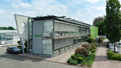Modernes zweistöckiges Bürogebäude mit Glasfassade, außenliegenden Lamellen und begrüntem Vorgarten an einer ruhigen Straße
