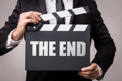 Mann im Anzug hält eine Filmklappe mit der Aufschrift „THE END“ vor der Brust