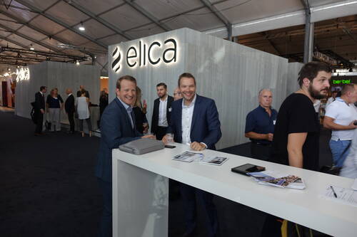 Geschäftsleute unterhalten sich gut gelaunt an einem Stehtisch vor dem beleuchteten Messestand von Elica in einer großen Ausstellungshalle