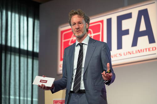 Geschäftsmann im Anzug präsentiert auf einer IFA-Bühne ein Miele-Produkt und spricht gestikulierend ins Publikum.