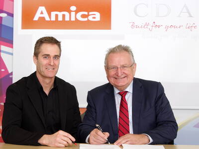 Zwei geschäftsmänner sitzen lächelnd an einem Tisch und unterzeichnen gemeinsam ein Dokument vor den Logos von Amica und CDA.