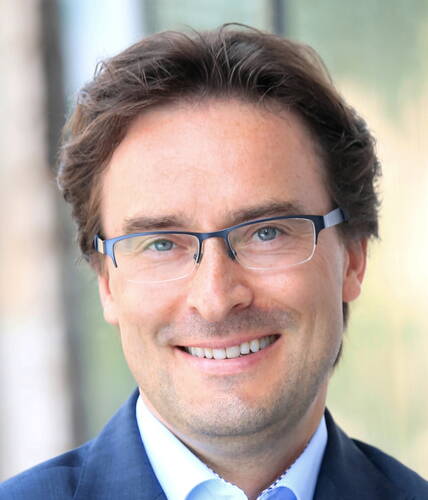 Lächelnder Mann mit Brille und blauem Anzug im Porträt vor unscharfem Hintergrund