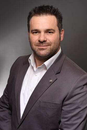 Mittelalterlicher Mann im grauen Anzug und weißem Hemd lächelt seriös vor neutral grauem Hintergrund in einem professionellen Porträt.