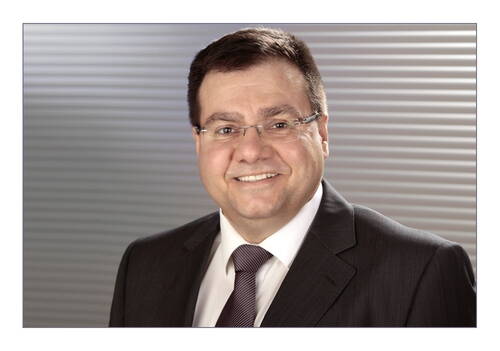 Lächelnder Geschäftsmann mit Brille im dunklen Anzug vor modernem, grauen Streifenhintergrund