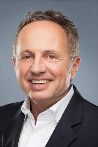 Lächelnder Mann mittleren Alters im Business-Anzug vor neutral grauem Hintergrund