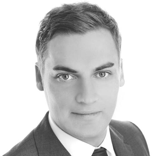 Junger Mann im Anzug mit Krawatte blickt direkt und ernst in die Kamera in einer Schwarzweiß-Portraitaufnahme.